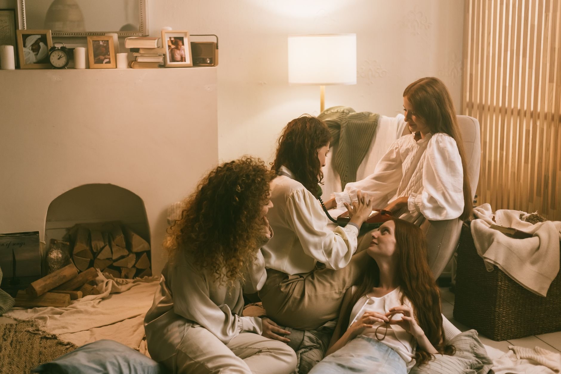 Four young women enjoying a cozy social gathering in warm lighting, creating a relaxed atmosphere of sisterhood