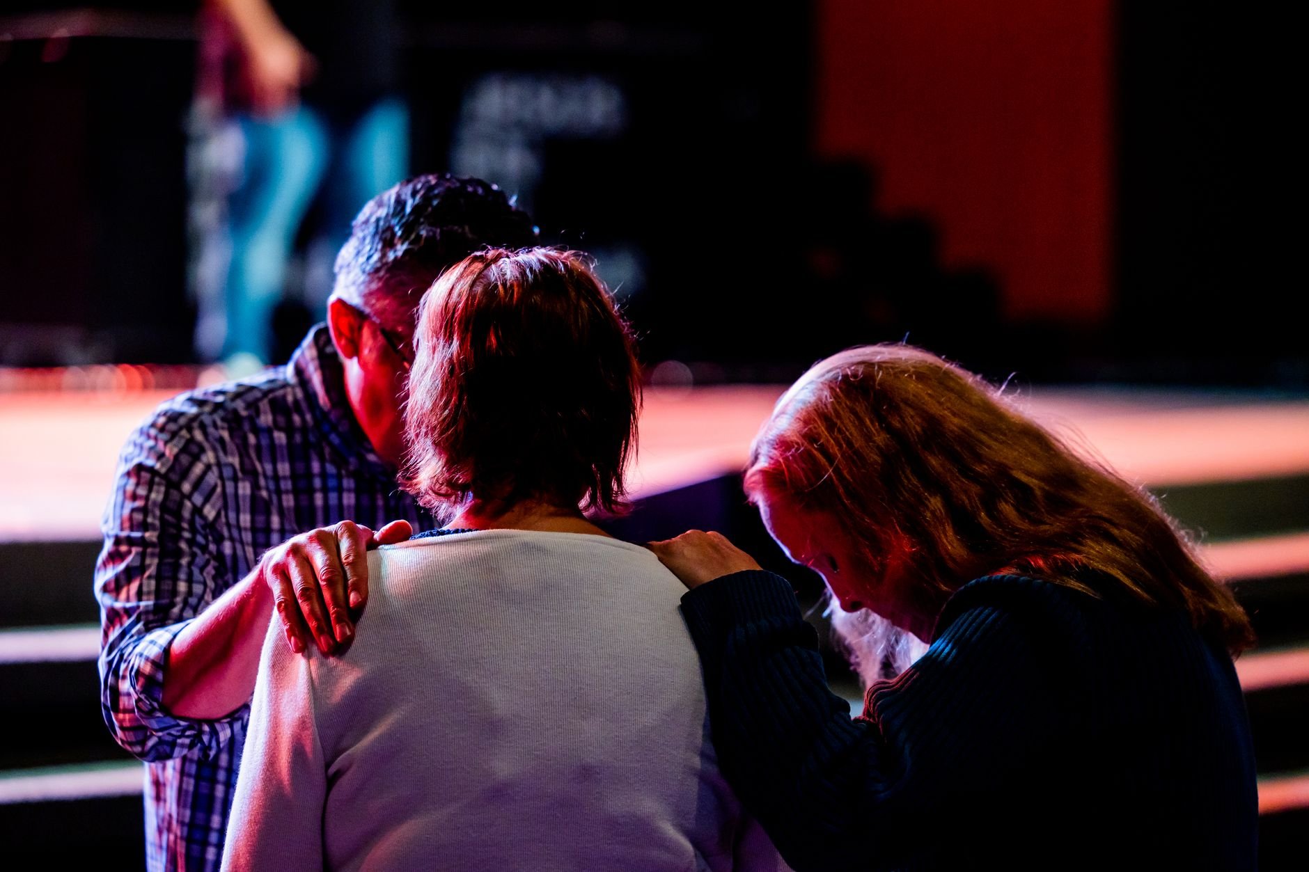 Three adults sharing a moment of prayer inside a warmly lit church gathering